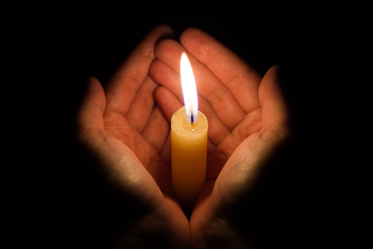 hands holding a burning candle in dark like a heart